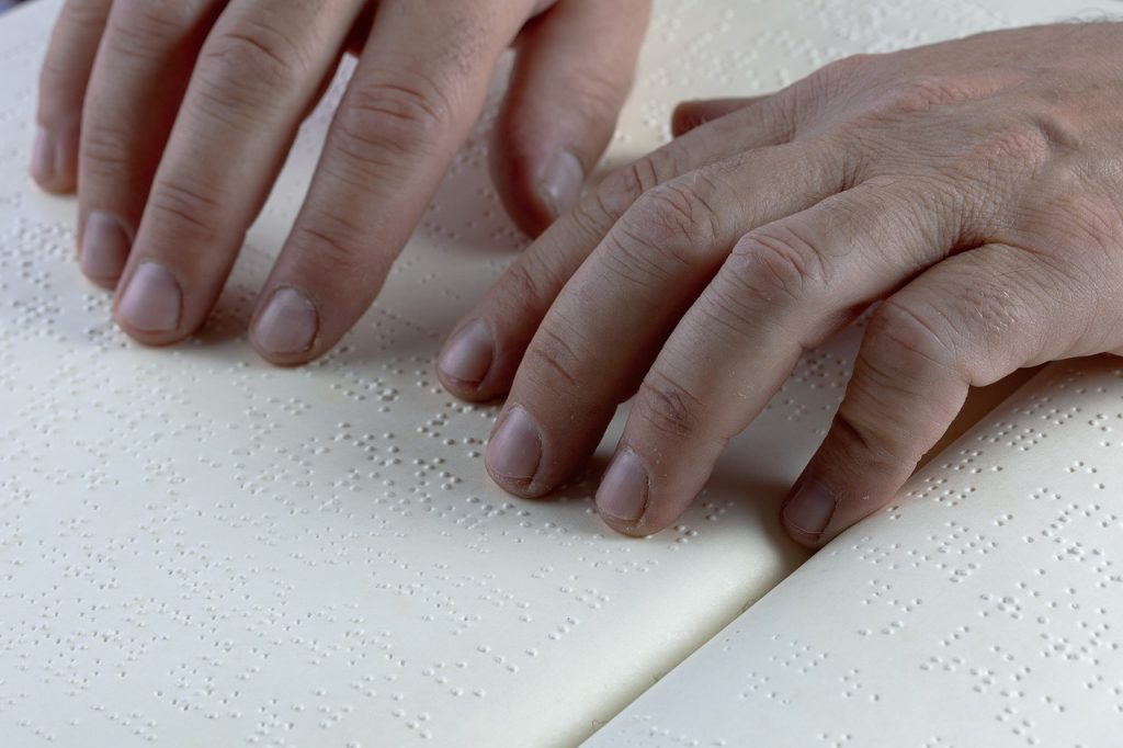 Mains d’une personne en train de lire un texte en braille, illustrant les défis d’accessibilité numérique pour les malvoyants ou personnes aveugles face aux sites internet encore inadaptés.