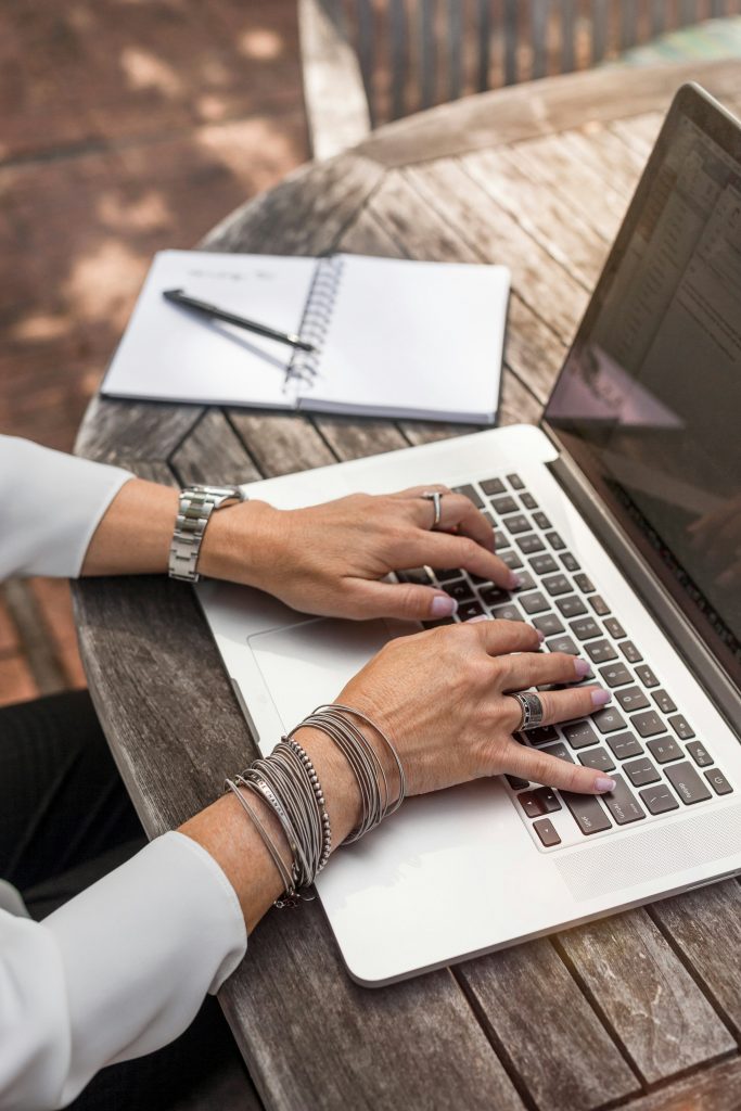 Femme en train de taper sur un ordinateur portable en extérieur. Cette image illustre un travail de recherche des nouvelles tendances 2025 SEO.