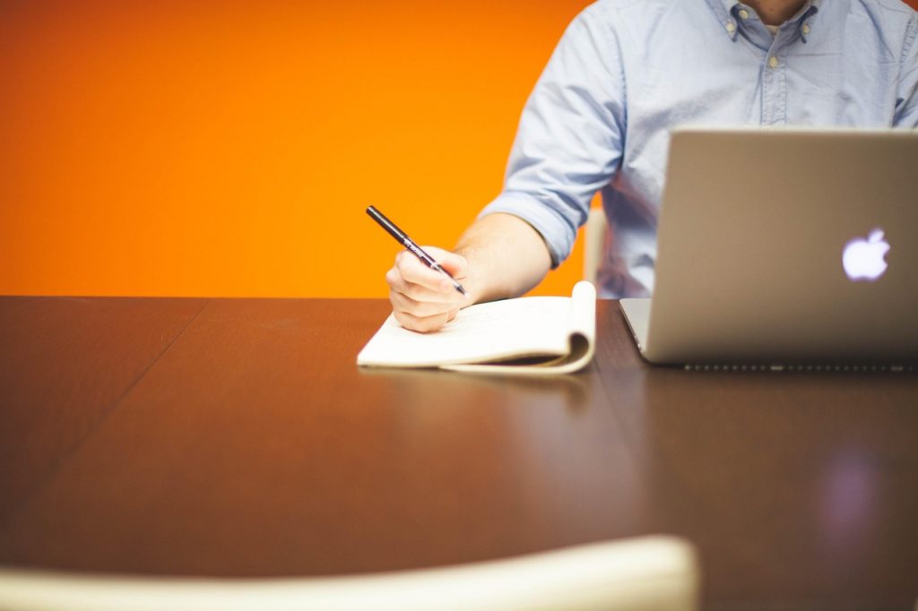 Rédacteur web en train de rédiger une fiche produit, carnet et ordinateur portable sur une table, symbole du travail de création de contenu SEO.