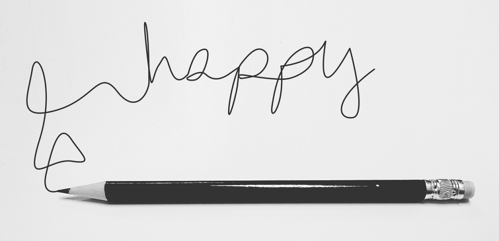 Crayon noir traçant le mot 'happy' en écriture cursive, symbolisant la créativité et les émotions dans l’acte d’écrire pour le SEO.